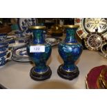 A small pair of Cloisonné vases on wooden stands in blue and green tones.