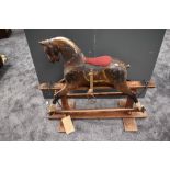 A traditional wooden painted Rocking Horse, missing mane and tail, having fitted saddle, on swing