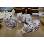 Three blue and white Burnham cat figures in different poses.