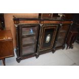 A large empire style ebonised cabinet, having central cupboard with painted enamelled plaque,
