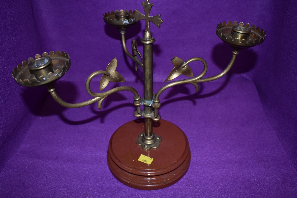 An arts and crafts brass candlestick holder having three swinging arms with ivy decoration and cross