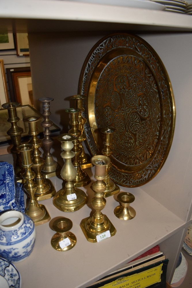 Eleven brass candlesticks and a embossed decorative wall plaque.