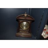 An ornate oak cased mantel clock with bevelled glass face and intricate metal decorations