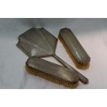 A silver dressing table hand mirror and two clothes brushes all having engine turned decoration,