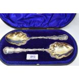 A cased pair of Edwardian silver fruit serving spoons having decorative scrolled rims and gilt