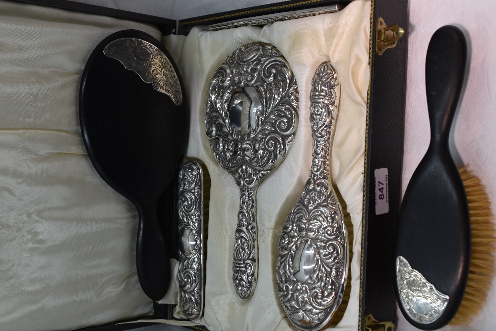 A cased silver four piece dressing table set having repousse mask, bird and scroll decoration,