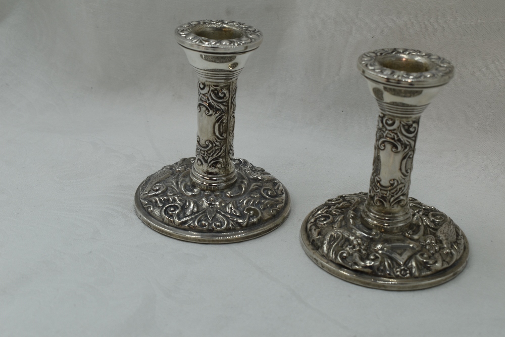 A pair of silver candle sticks of short form having bird and mask repousse decoration with plain