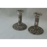 A pair of silver candle sticks of short form having bird and mask repousse decoration with plain