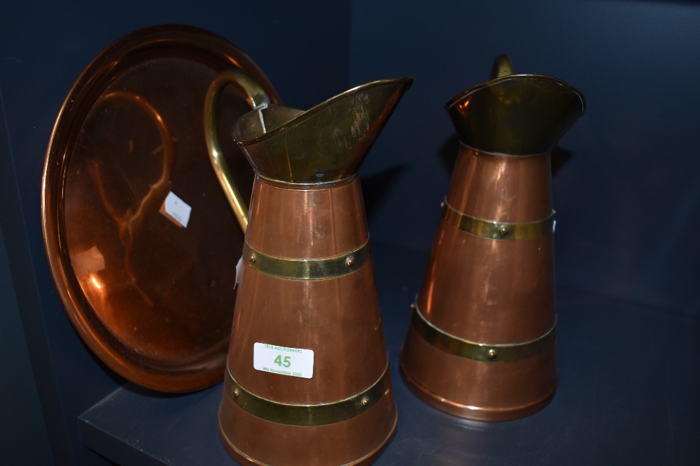 Two copper and brass pitchers and a copper charger.