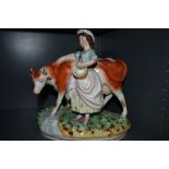 A Staffordshire style figurine depicting milk maid and cow.
