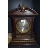 An ornate oak cased mantel clock with bevelled glass face and intricate metal decorations