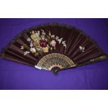 A late 19th/early 20th century maroon silk fan, satin leaf embroidered with basket of flowers and