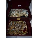 A maroon coloured jewellery box containing a selection of costume jewellery chains and beads