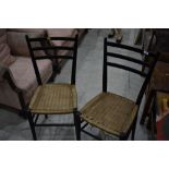 A pair of ebonised rail back dining chairs having strung seats