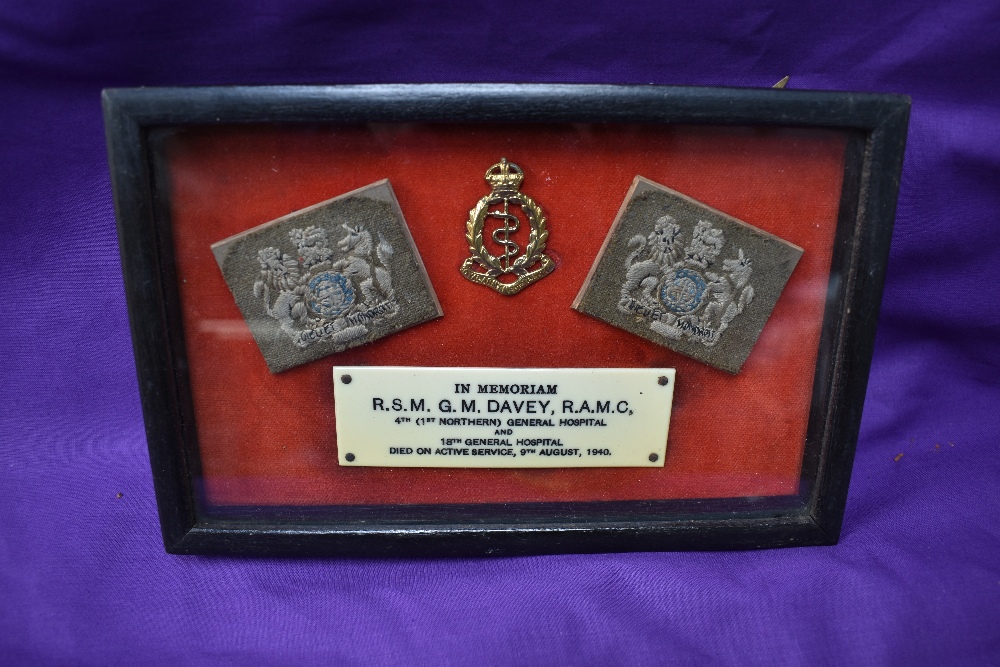 A framed WW2 Memorial consisting of two shoulder badges, cap badge and plaque reading In Memoriam