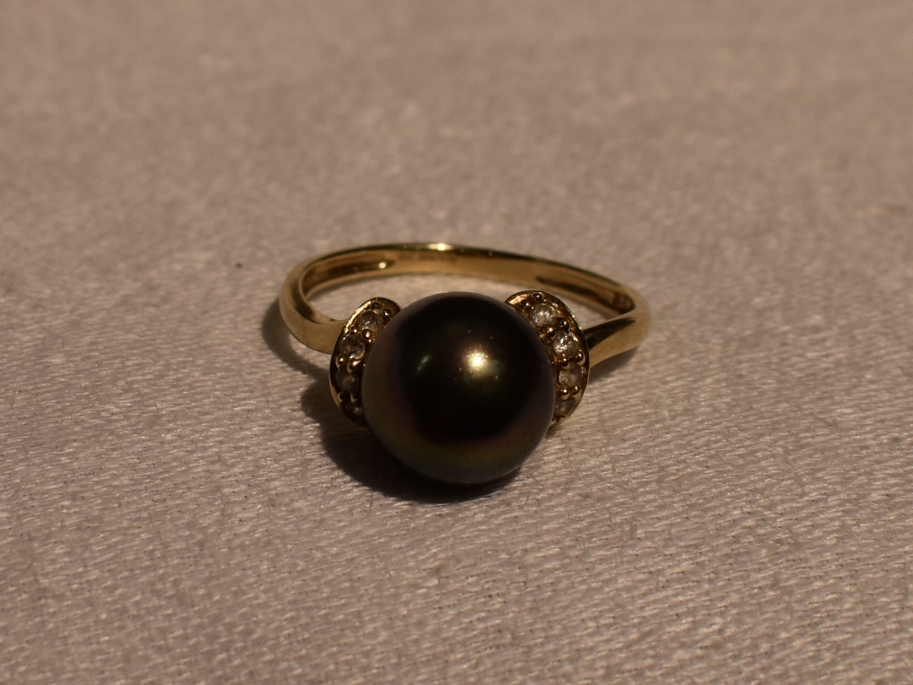 A lady's dress ring having a simulated black pearl flanked by cubic zirconias on a 14ct gold loop,