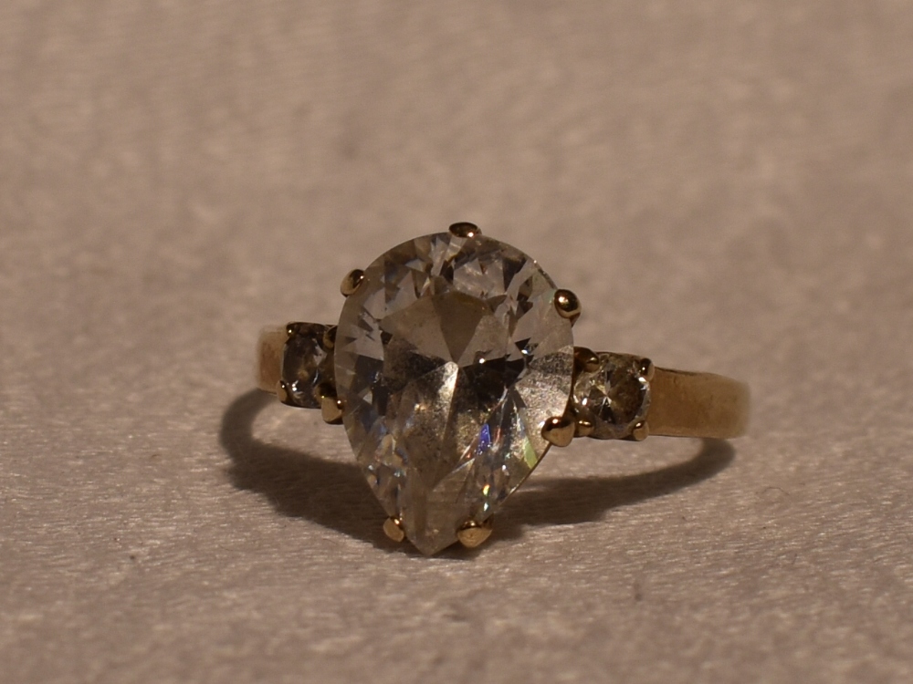 A lady's dress ring having a teardrop cut cubic zirconia flanked by a round cut CZ to each