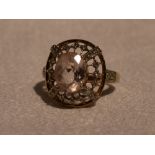 A lady's dress ring having a morganite style oval stone within an open border having diamond chip