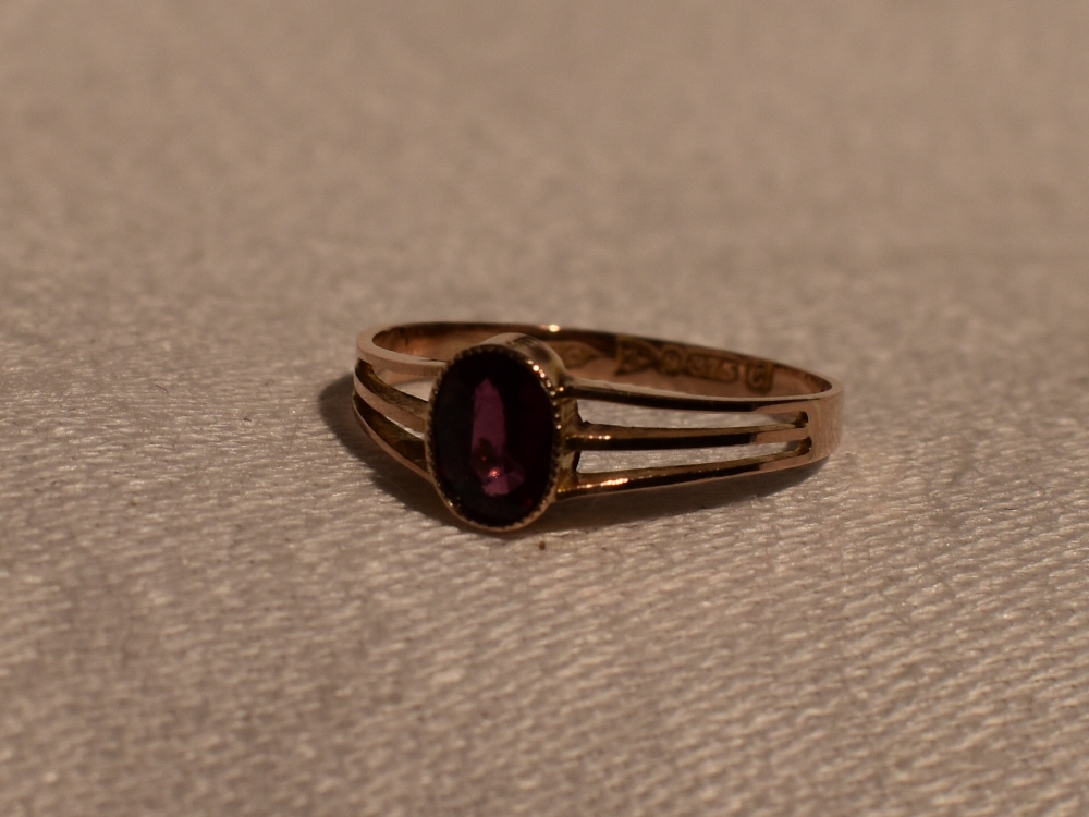 A lady's dress ring having an oval ruby style stone in a collared mount to open triple bar shoulders