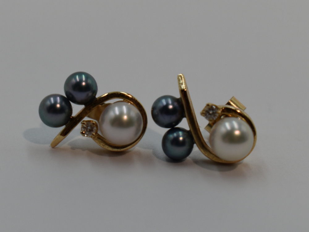 A pair of cultured black and white pearl stud earrings with diamond chip decoration in yellow