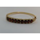 A 9ct gold hinged bangle set with nine oval garnets interspersed by pairs of diamond chips in a