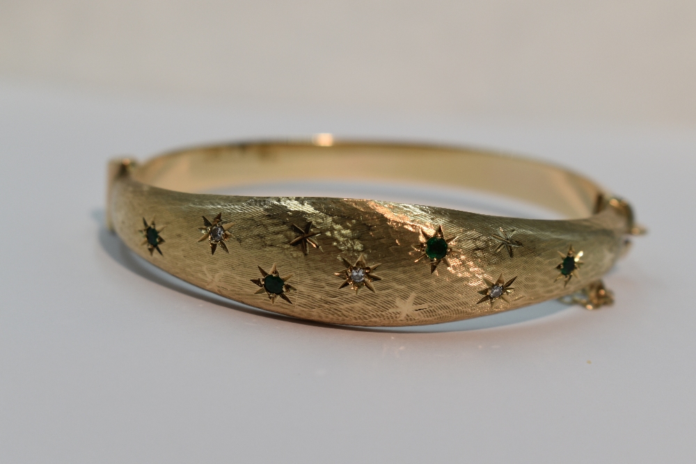 A 9ct gold hinged bangle having diamond and emerald chip decoration in star burst settings on