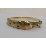 A 9ct gold hinged bangle having diamond and emerald chip decoration in star burst settings on