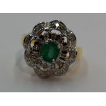 A lady's dress ring having a central emerald within a frilled double cluster of small diamonds in