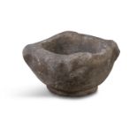 A MEDIEVAL GRANITE MORTAR, carved to each side with a human mask on short circular foot. 21cm
