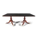 A GEORGE III STYLE MAHOGANY EXTENDING DINING TABLE, on twin pillar supports with tripod bases and