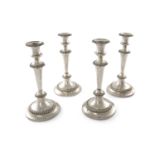 A SET OF FOUR SHEFFIELD PLATED CIRCULAR CANDLESTICKS, with urn shaped nozzles, gadrooned banded