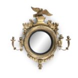 A GEORGE IV GILTWOOD CONVEX GIRANDOLE MIRROR, surmounted by a carved eagle flanked by leaf sprays,