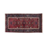 A SMALL CAUCASIAN WOOL RUG, the iron red ground decorated with geometric motifs within a blue and