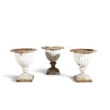 A SET OF THREE VICTORIAN CAST IRON URNS, the flared rims with leaf cast banding, above lobed