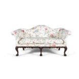 A GEORGIAN STYLE MAHOGANY FRAMED CAMEL BACK COUCH, covered in floral pattern on cream ground