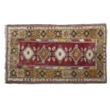 A Turkish wool rug, the deep red central field with five medallions within border and guard stripes.