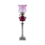 A SILVER PLATED CORINTHIAN COLUMN OIL TABLE LAMP, with ruby glass reservoir. 84cm high overall