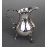 A George V silver cream jug of baluster shape, with card-cut rim, scroll handle & three pad feet,