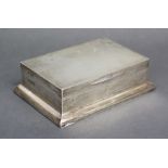 A silver rectangular cigarette box with hinged lift lid & on wide base; London 1913 by Blackmore &