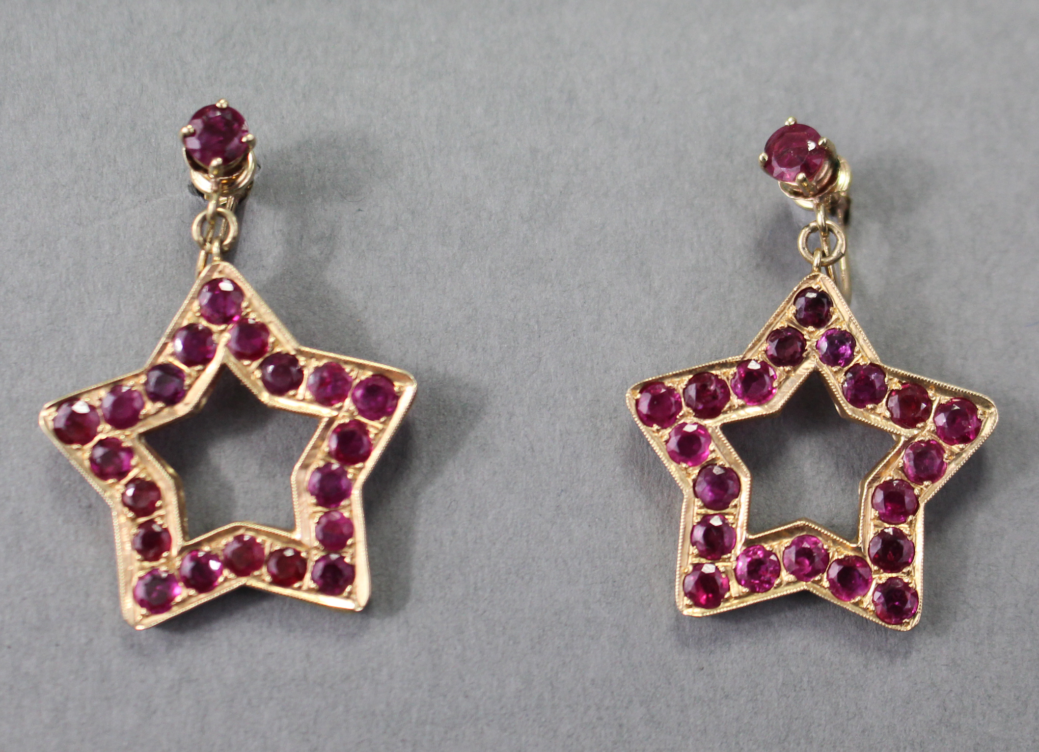 A PAIR OF RUBY PENDANT EARRINGS, each of open five-pointed star shape set twenty round-cut stones of