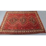 A Persian carpet of crimson ground, with three central lozenges surrounded by geometric motifs, &