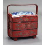 A Japanese lacquered bento box of three stacking tiers, red ground with stylised floral decoration &