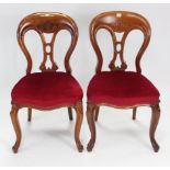 A pair of mid-Victorian mahogany dining chairs with rounded open backs, padded seats, & on carved