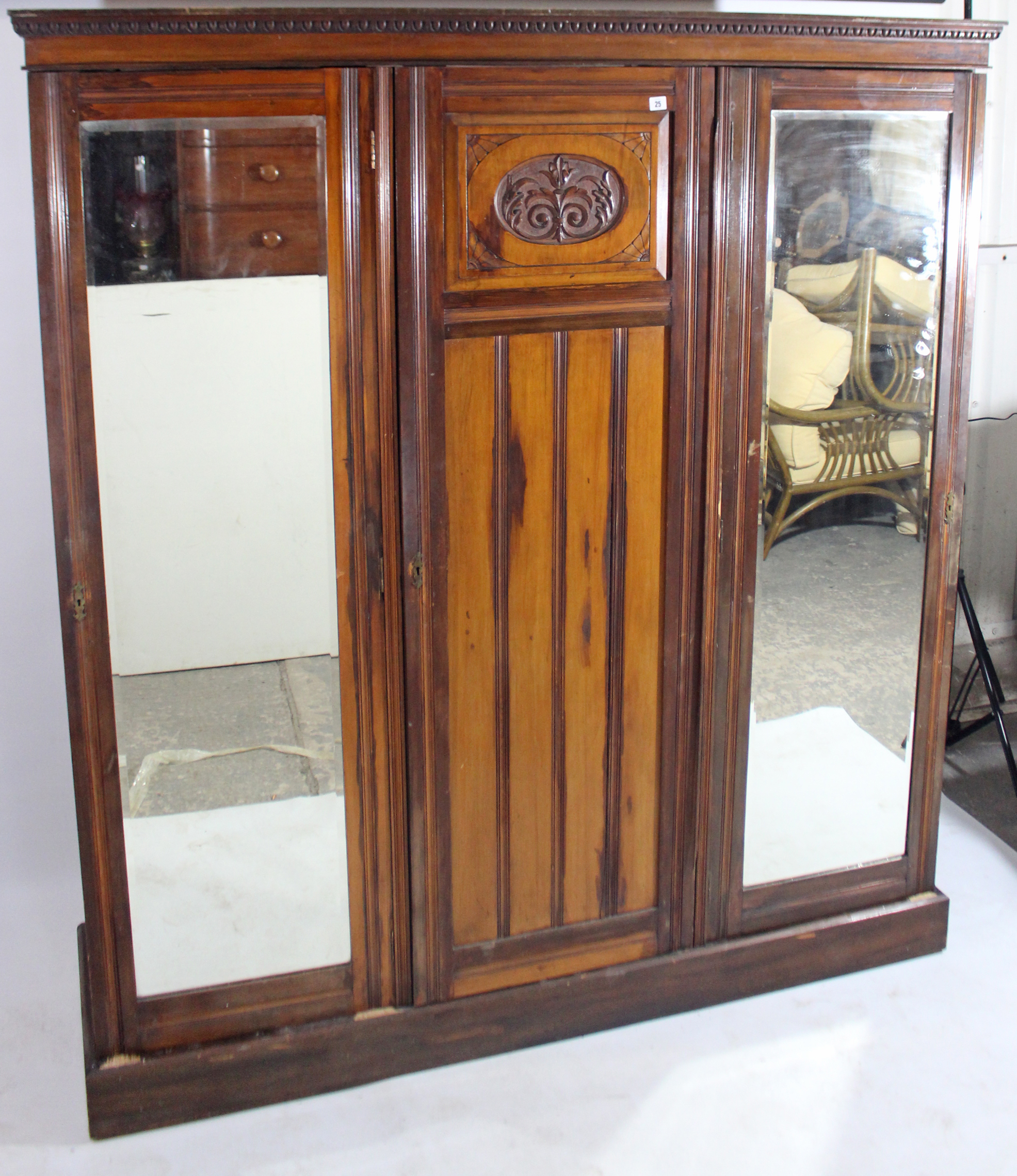 An Edwardian walnut wardrobe with moulded cornice, having fitted interior enclosed by carved panel