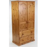 A pine wardrobe enclosed by pair of fielded panel doors above two long drawers, & on shaped plinth
