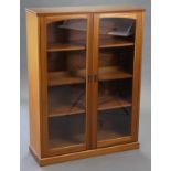 A teak bookcase, fitted three shelves enclosed by pair of glazed doors, & on plinth base, 34½”