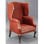 A Queen Anne style wing-back armchair, with shaped back & sides, scroll arms, & sprung seat