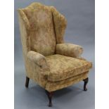 An upholstered wing-back armchair in the early 18th century style, with padded squab cushion, & on