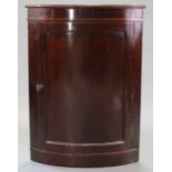 An early 19th century mahogany bow-front hanging corner cupboard, with moulded cornice above two