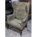 A Victorian wing-back armchair (requires re-upholstery), on bobbin-turned legs & ceramic castors.